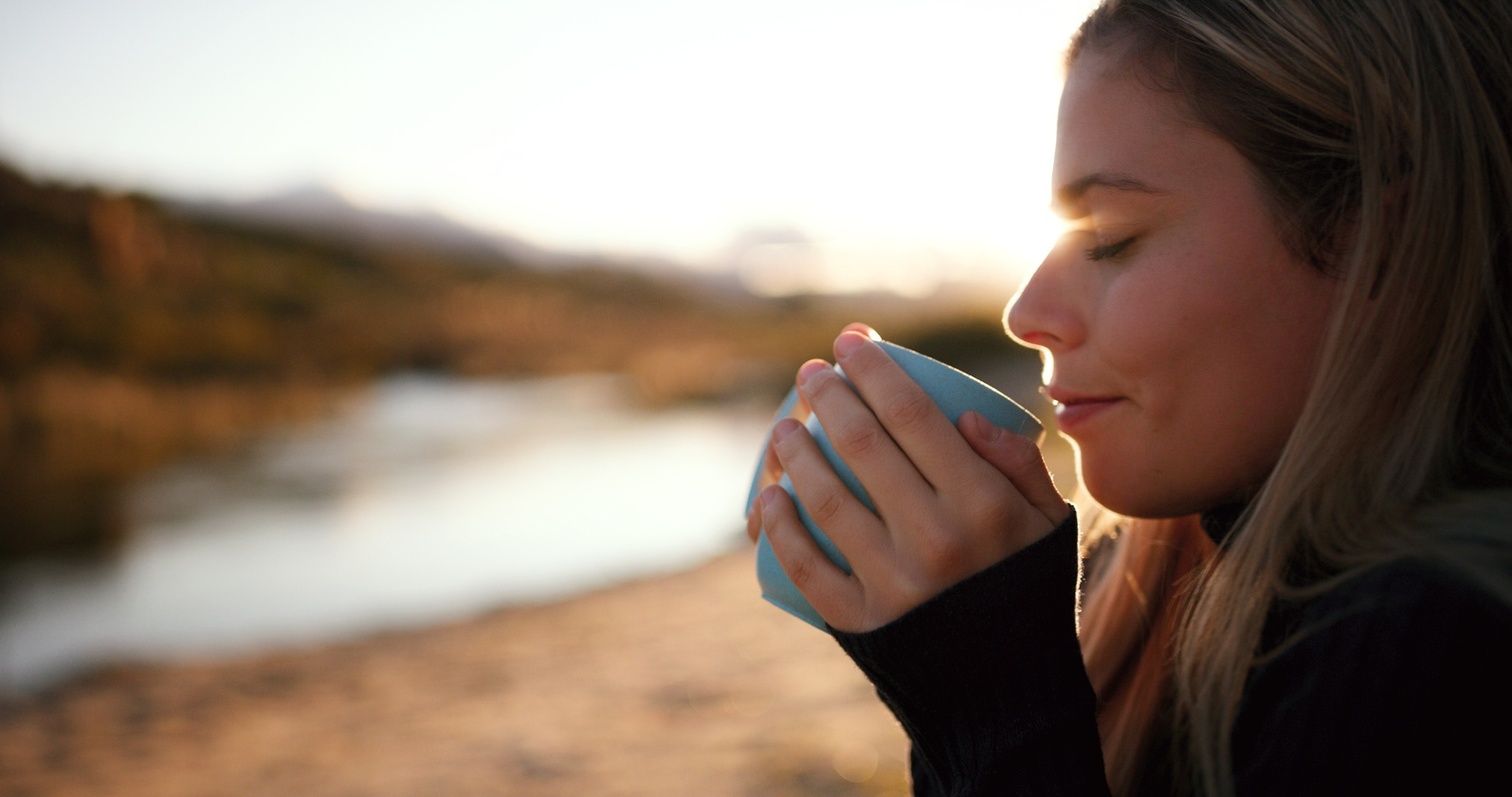 Woman, relax and camp coffee by river water in morning in summer by lake. Calm, young female person and tea at sunrise on holiday, travel and vacation with hot drink and freedom from camping outdoor